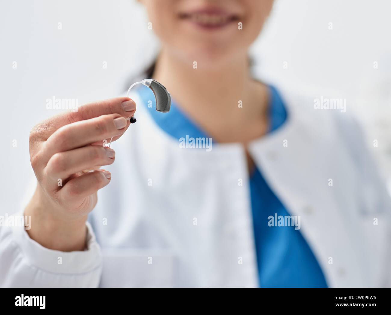 Modernes Hörgerät in den Händen lächelnder Audiologen, Nahaufnahme, Weichfokus. Hörgeräte, Hörlösungen Stockfoto