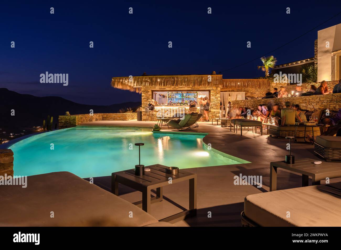 IOS, Griechenland - 17. September 2023 : Blick auf verschiedene Personen, die vor einem Pool in einer Lounge Bar sitzen und den Sonnenuntergang in iOS Griechenland genießen Stockfoto