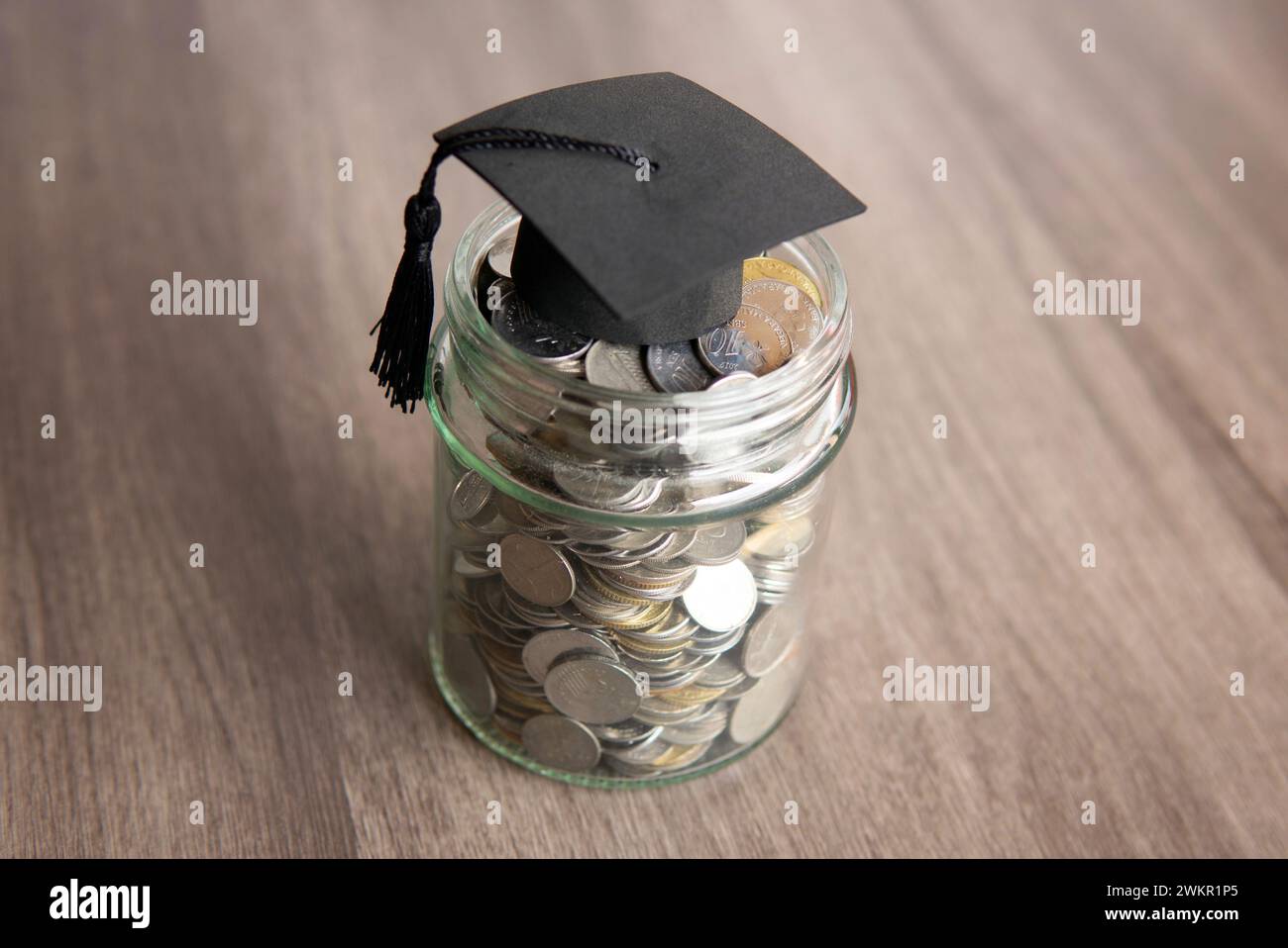 Glasgefäß gefüllt mit Münzen und einer Graduierungskappe darauf. Kopierbereich für Text. Einsparungskonzept im Bildungsbereich. Stockfoto