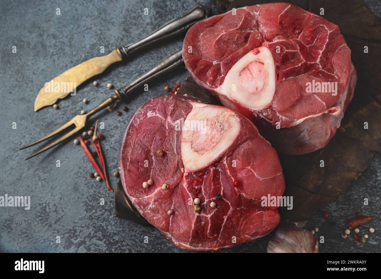 Roher Ossobuco. Kalbsschinken Ossobuco mit Pfeffer, Zitrone und Knoblauch für Gremolata, typische Zutaten der italienischen lombardischen Küche, Blick von oben auf dunklem Hintergrund Stockfoto