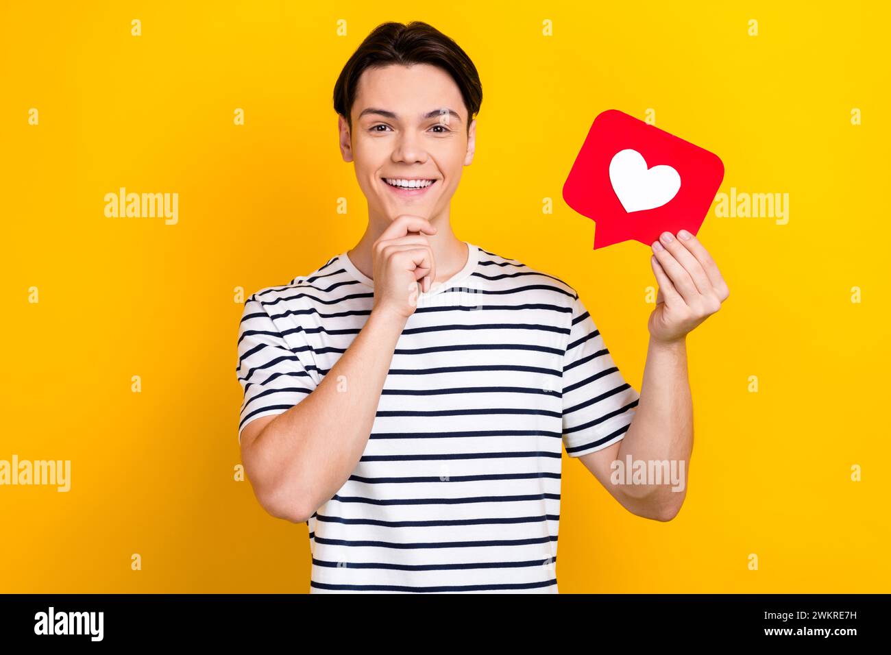 Porträt eines gesinnten Studenten mit brünetten Haaren tragen stilvolles T-Shirt halten wie Postard Finger auf dem Kinn isoliert auf gelbem Hintergrund Stockfoto