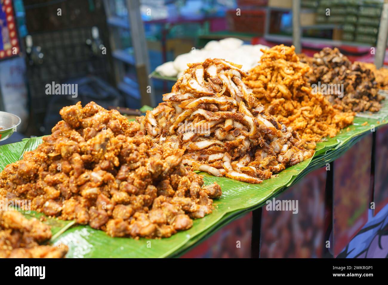 Eine verlockende Auswahl an thailändischem Streetfood mit gehäuften Haufen knusprigem Schweinefleisch auf Bananenblättern, die die reiche Vielfalt an Texturen und Aromen zeigen, Stockfoto