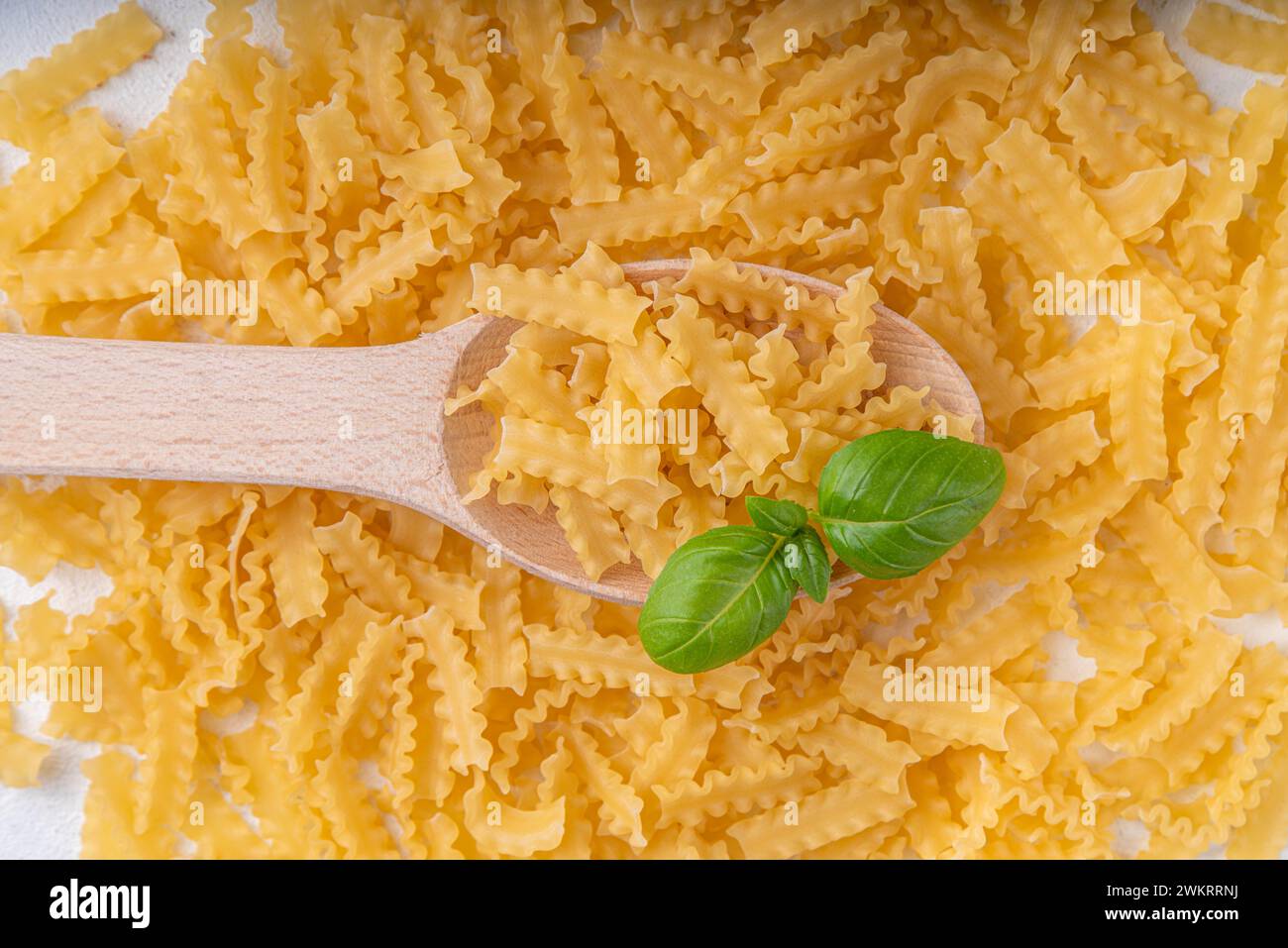 Rohe, ungekochte Mafaldine-Nudeln mit Zutaten zum Kochen. Kurze italienische Mafaldine-Pasta mit Olivenöl, Kirschtomaten, Basilikum und Gewürzen auf weißer Küche Stockfoto