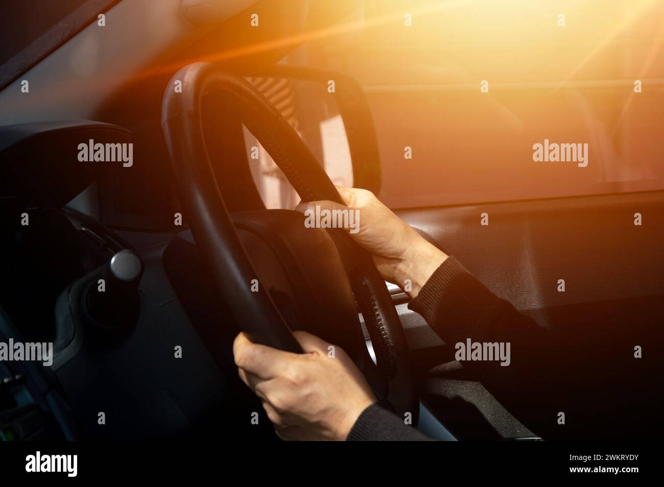 Mann, der Auto fährt, Hand am Lenkrad, Blick auf die Straße vor uns, Sonnenuntergang. Stockfoto