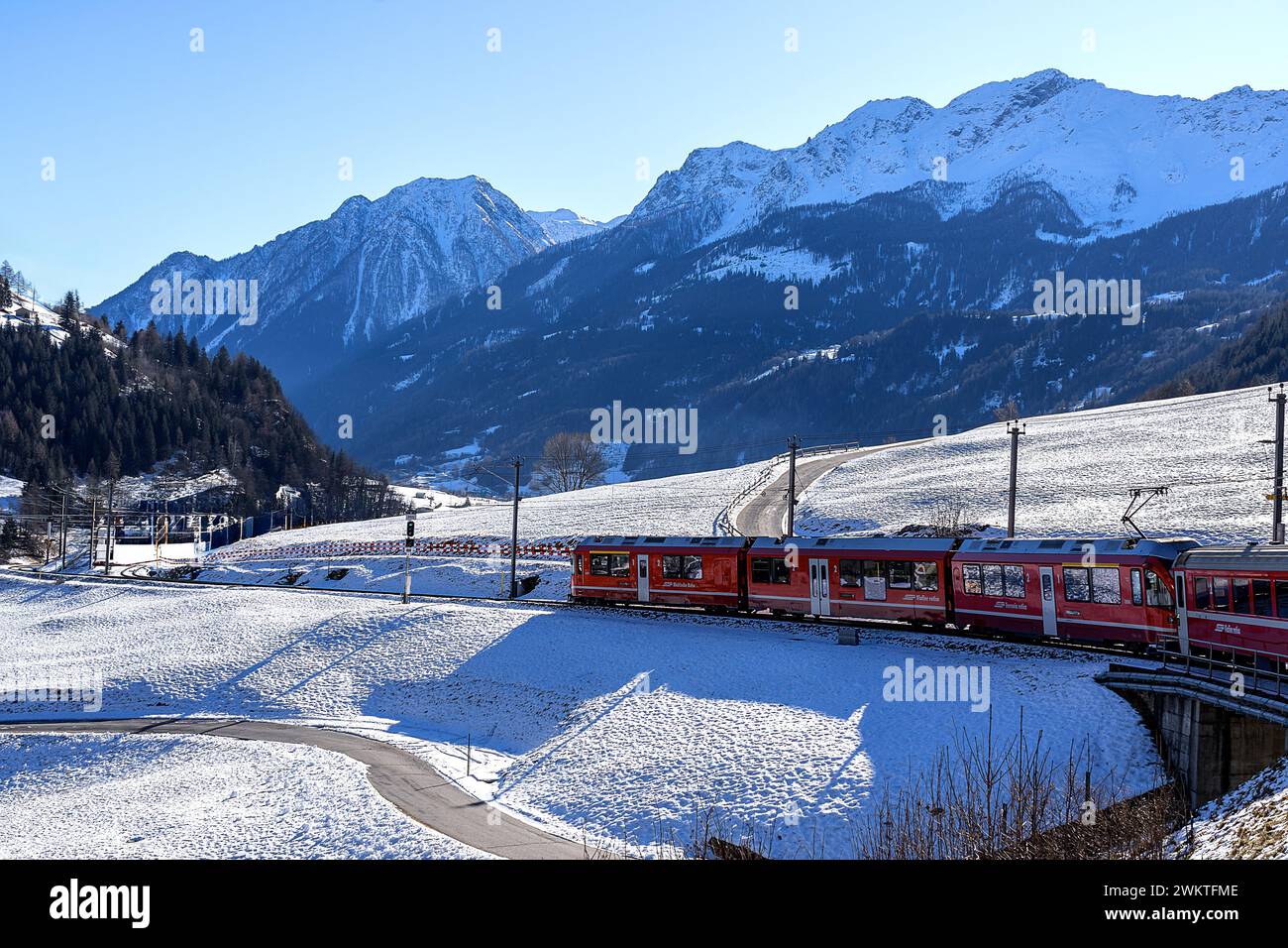 schweiz, 13.01.2024: Der zum UNESCO-Weltkulturerbe gehörende Rote Zug Bernina fährt langsam vorwärts durch den Schnee im Schatten der Nadelbaumdecke Stockfoto