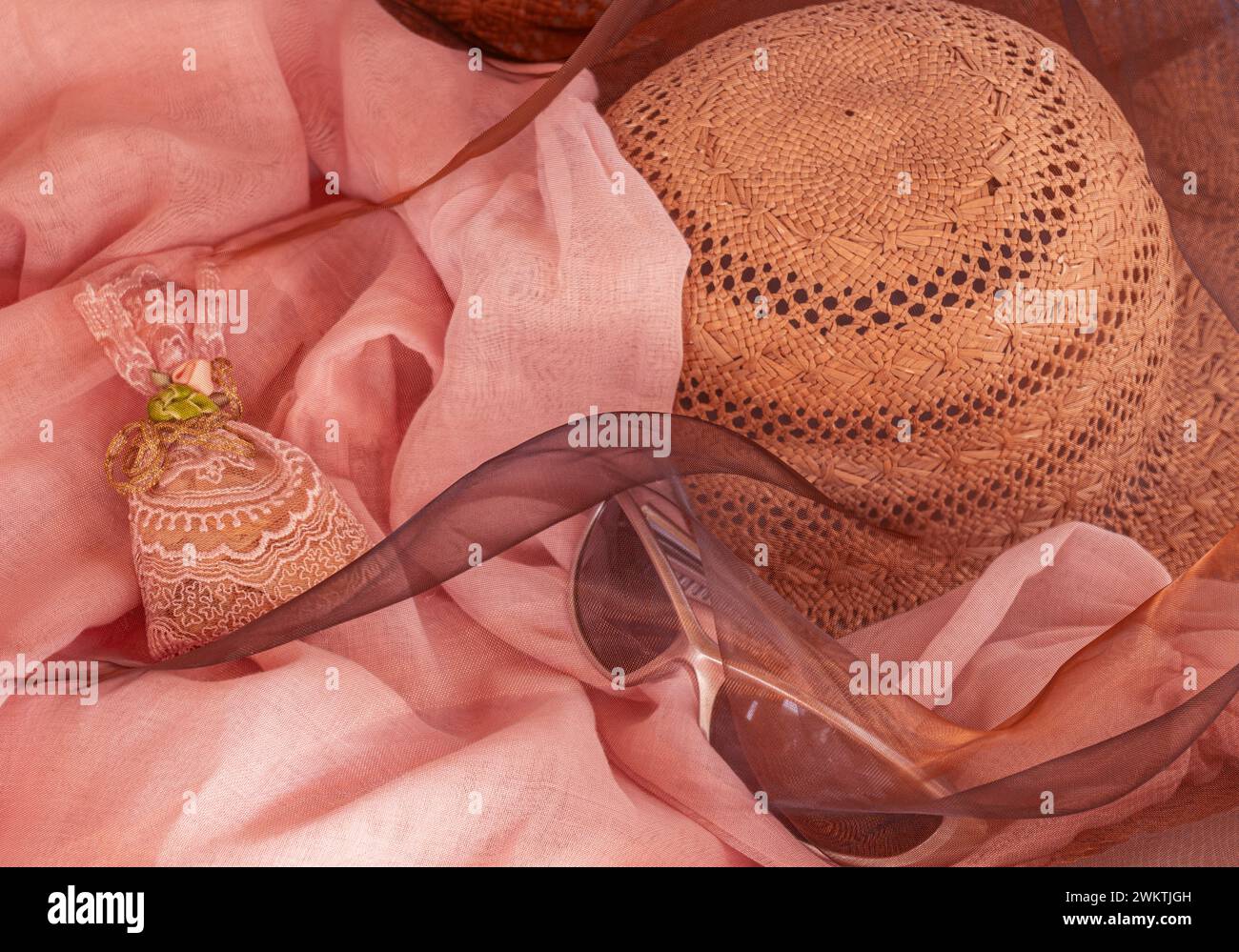 Romantischer rosafarbener Sonnenhut, Sonnenbrille, Organdystoff und Brokatbeutel, wie für Urlaub, Entspannung oder Feier im femininen Stil. Stockfoto