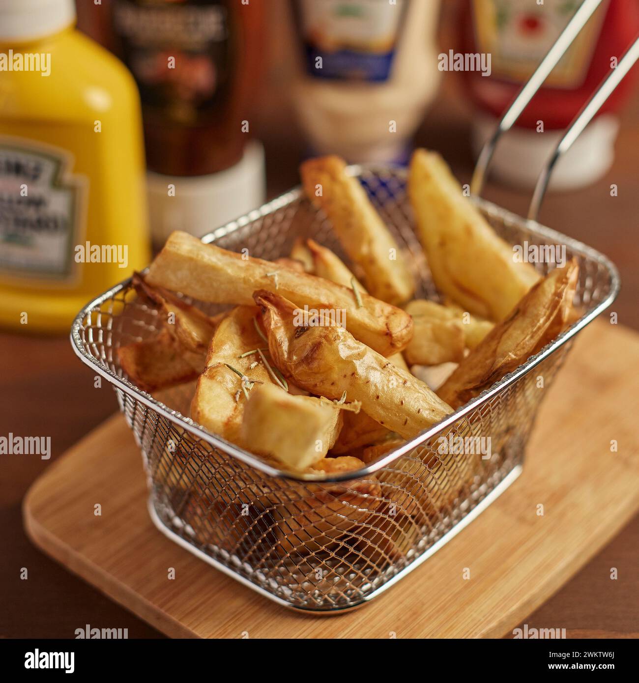 Französische Pommes Frites im Landhausstil in einem Metallkorb und Gewürze im Hintergrund Stockfoto
