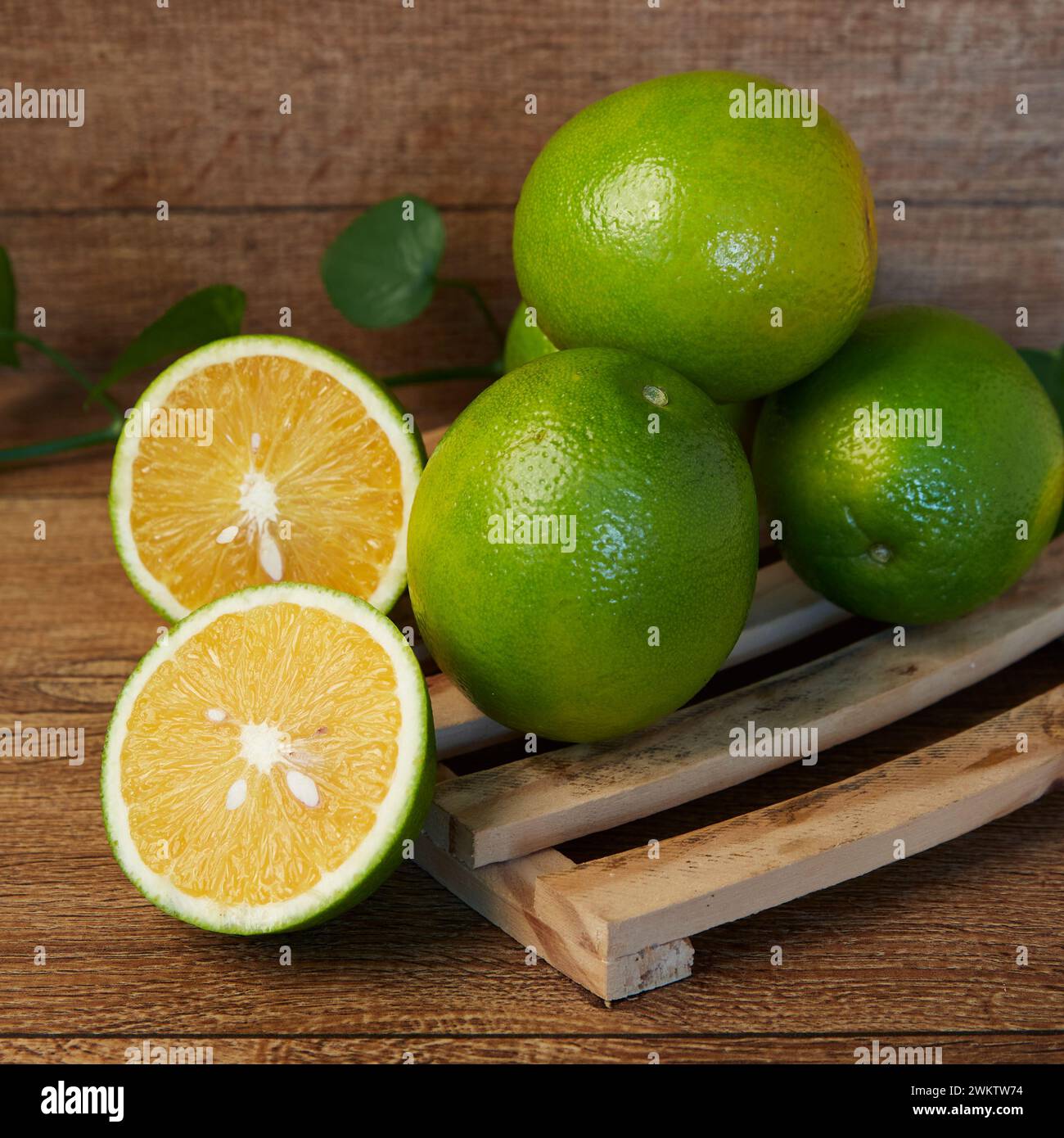 Eine frische Limette und Orangenhälften auf Holztablett mit grünen Blättern Stockfoto