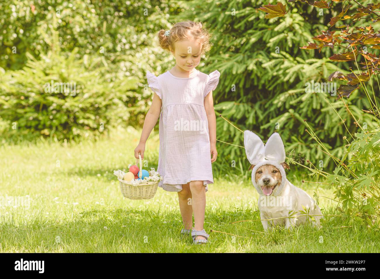 Familie Ostereierjagd. Mädchen und Hund sammeln bunte Eier in der Pfanne Stockfoto