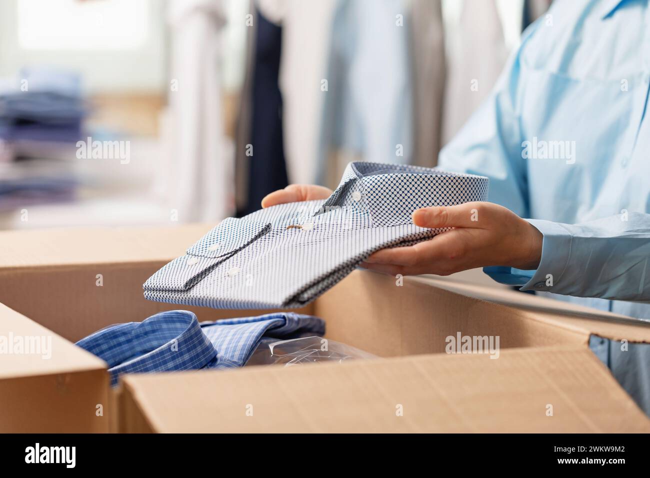 Ein Modedesigner steckt ein gefaltetes Hemd in eine Box, um es an einen Kunden zu schicken, eine Frau schickt Kleidung an Marktplätze, arbeitet zu Hause Stockfoto