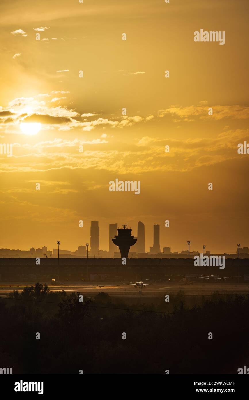 Panoramablick auf das Terminal T4 des Flughafens Madrid Barajas in der Abenddämmerung, mit der Skyline der Stadt und ihren vier Wolkenkratzern im Hintergrund. Stockfoto