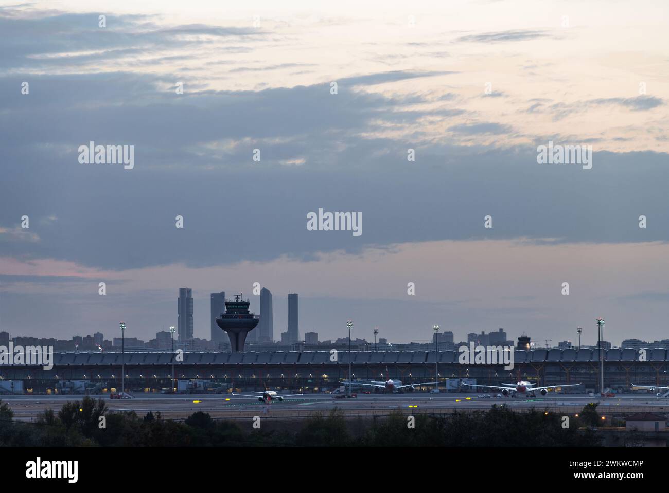 Panoramablick auf das Terminal T4 des Flughafens Madrid Barajas in der Abenddämmerung, mit der Skyline der Stadt und ihren vier Wolkenkratzern im Hintergrund. Stockfoto