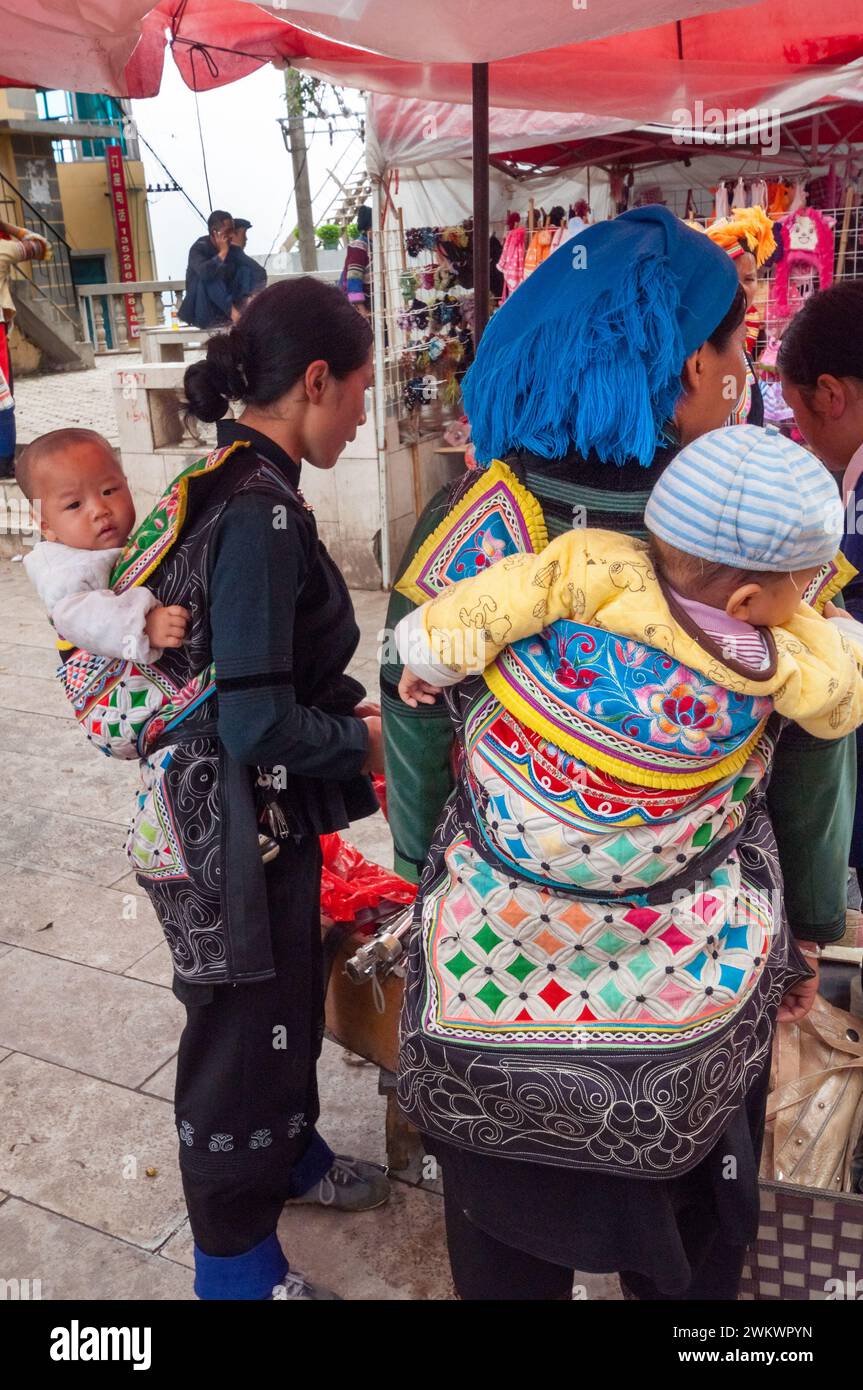 Zwei Frauen aus der ethnischen Minderheit Hani mit Babytragen auf dem Rücken, die auf einem lokalen Markt in Yuanyang, Yunnan, China, einkaufen Stockfoto