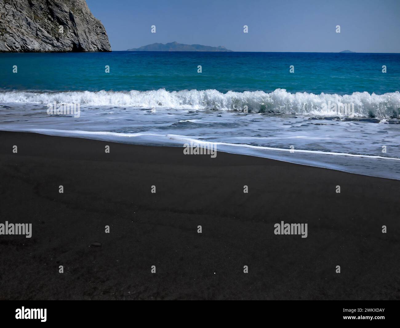 Die schwarze felsige Strandfarbe steht im Kontrast zum klaren hellblauen Wasser der Ägäis, gegenüber dunklem und hellem Ton, Santorini Island, Griechenland, Stockfoto