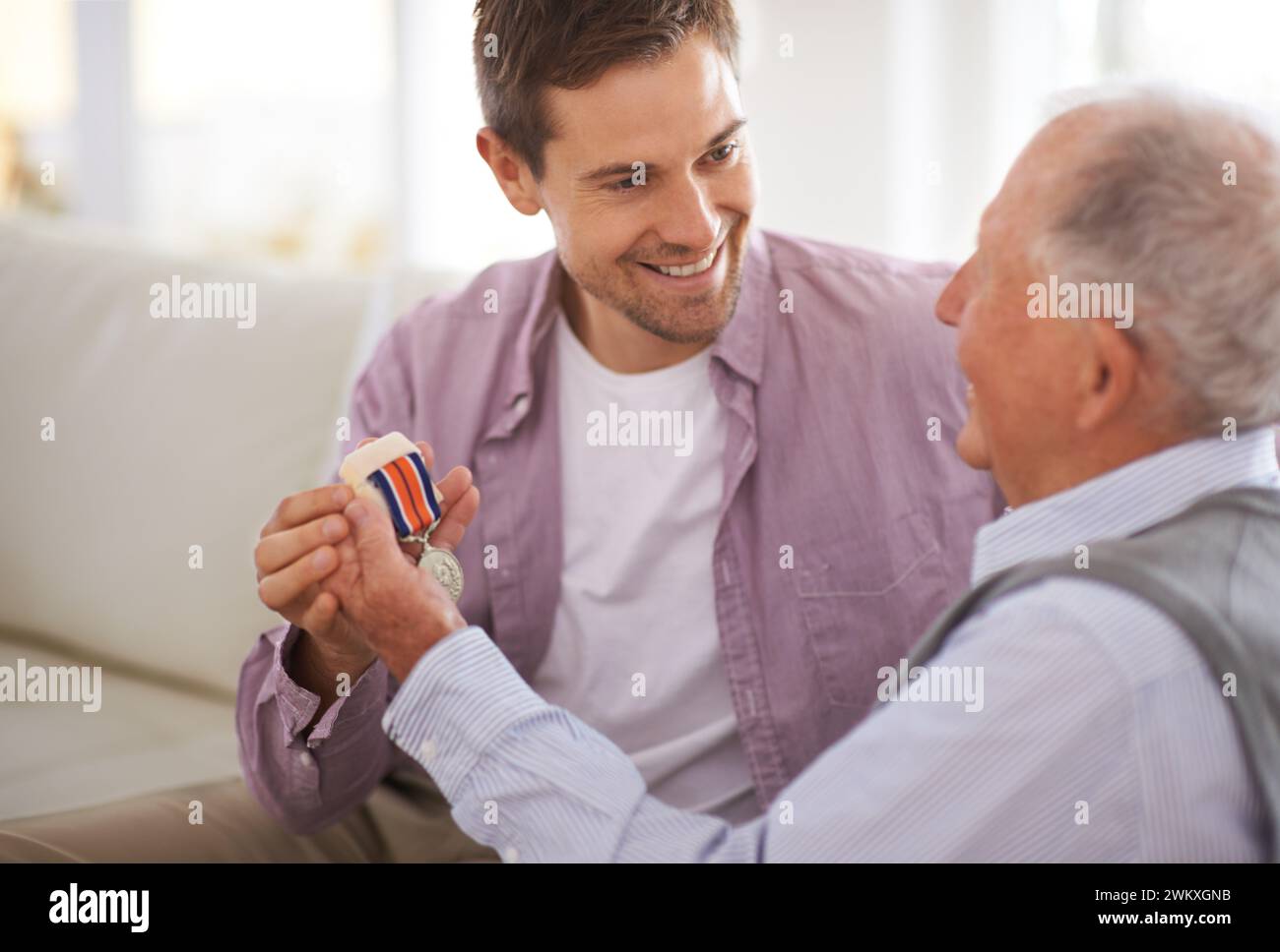 Senior, Mann und Sohn oder Medaille auf Sofa mit Kriegsabzeichen, Stolz und Ehre für den Militärhelden im Wohnzimmer. Älterer, Veteran und pensionierter Soldat Stockfoto