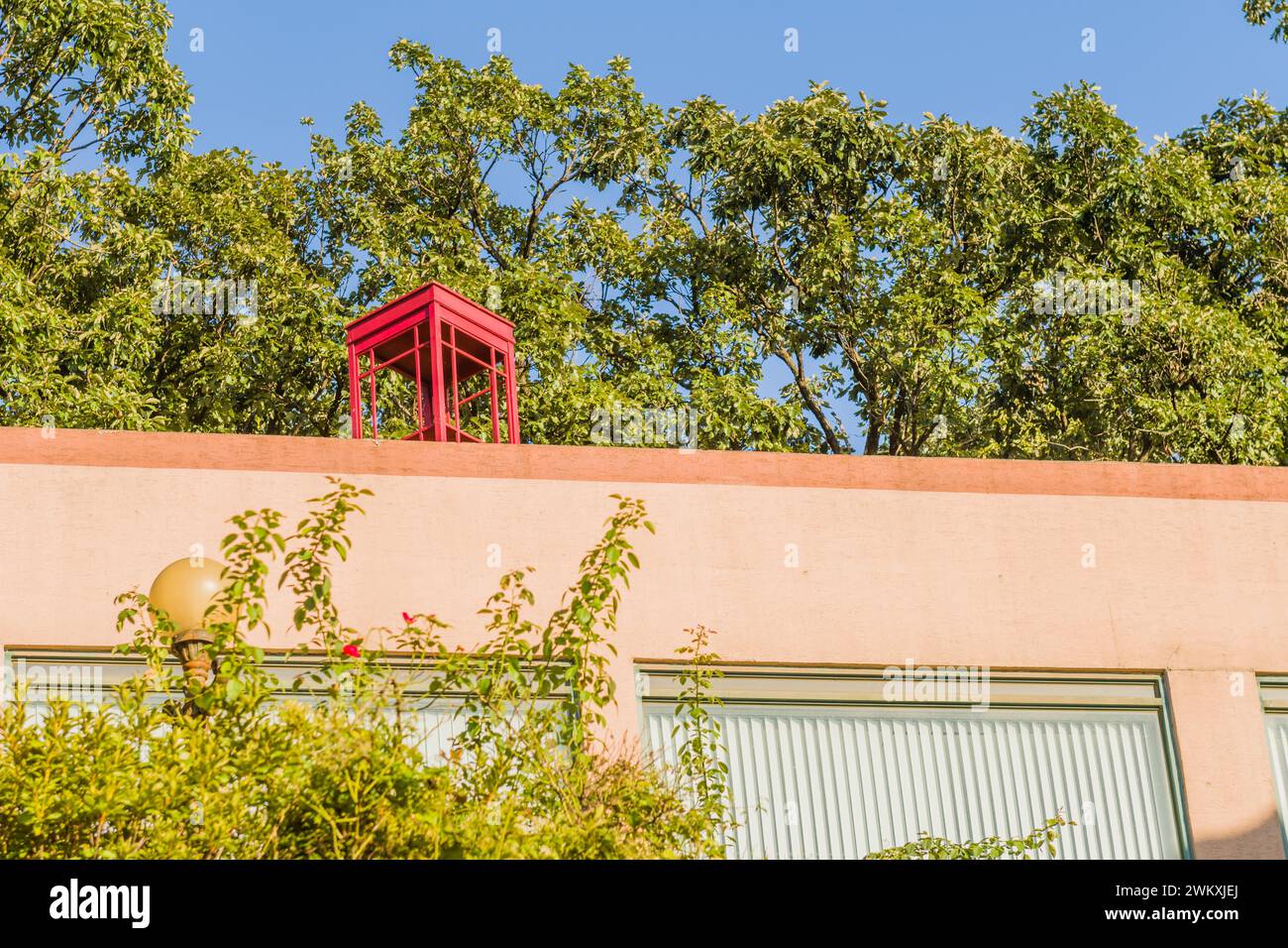 Rote hölzerne Telefonzelle ohne Glas auf dem pinkfarbenen Stuckgebäude am sonnigen Tag mit blauem Himmel in Südkorea Stockfoto