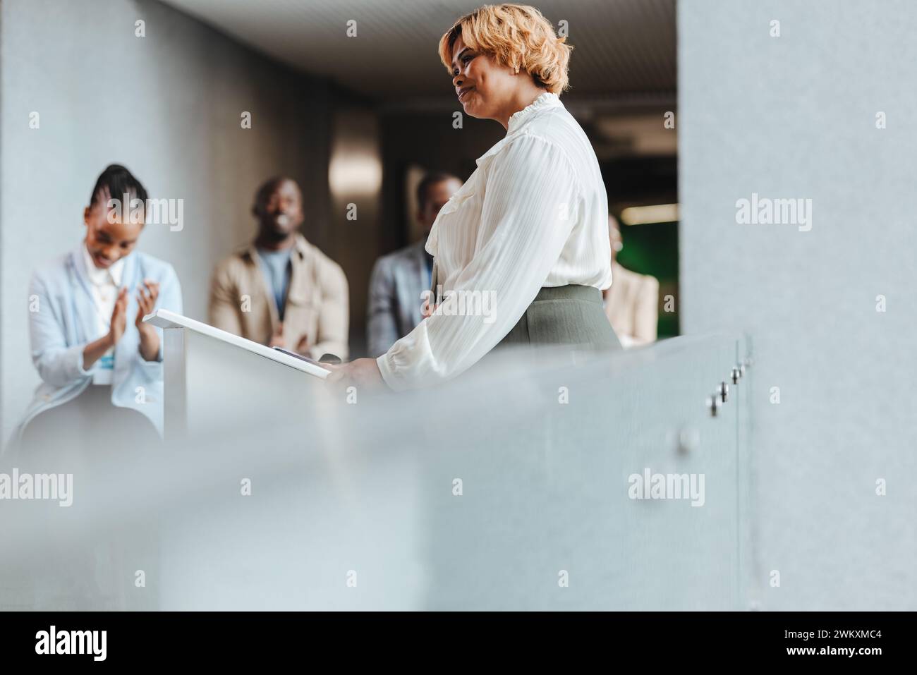 Glückliche Geschäftsfrau, die während eines Seminars von Kollegen Applaus erhält, symbolisiert Anerkennung, Erfolg und berufliche Entwicklung. Youn Stockfoto