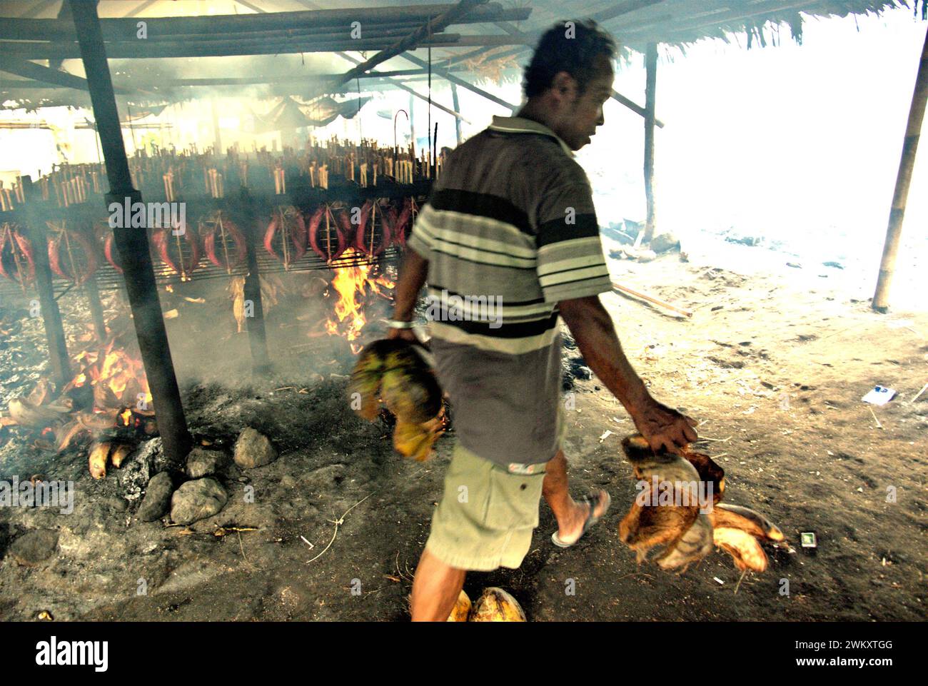 Ein Arbeiter bringt Kokosnussschalen mit, die als Brennstoff zum Räuchern von Bonito-Thunfischfleisch in einer Heimindustrie in Bitung, Nord-Sulawesi, Indonesien, verwendet werden. Der Beitrag indigener Wissens zur technologischen Innovation bietet laut dem Bericht des Zwischenstaatlichen Ausschusses für Klimaänderungen (IPCC) aus dem Jahr 2023 eine breite Palette von Optionen für das Management unter anderem der Ernährungssicherheit. Der im Volksmund als Cakalang Fufu bekannte geräucherte Thunfisch gilt als exotisches einheimisches Lebensmittel und könnte eine alternative Lösung für den Umgang mit den Auswirkungen des Klimawandels auf den Ozean werden. Stockfoto