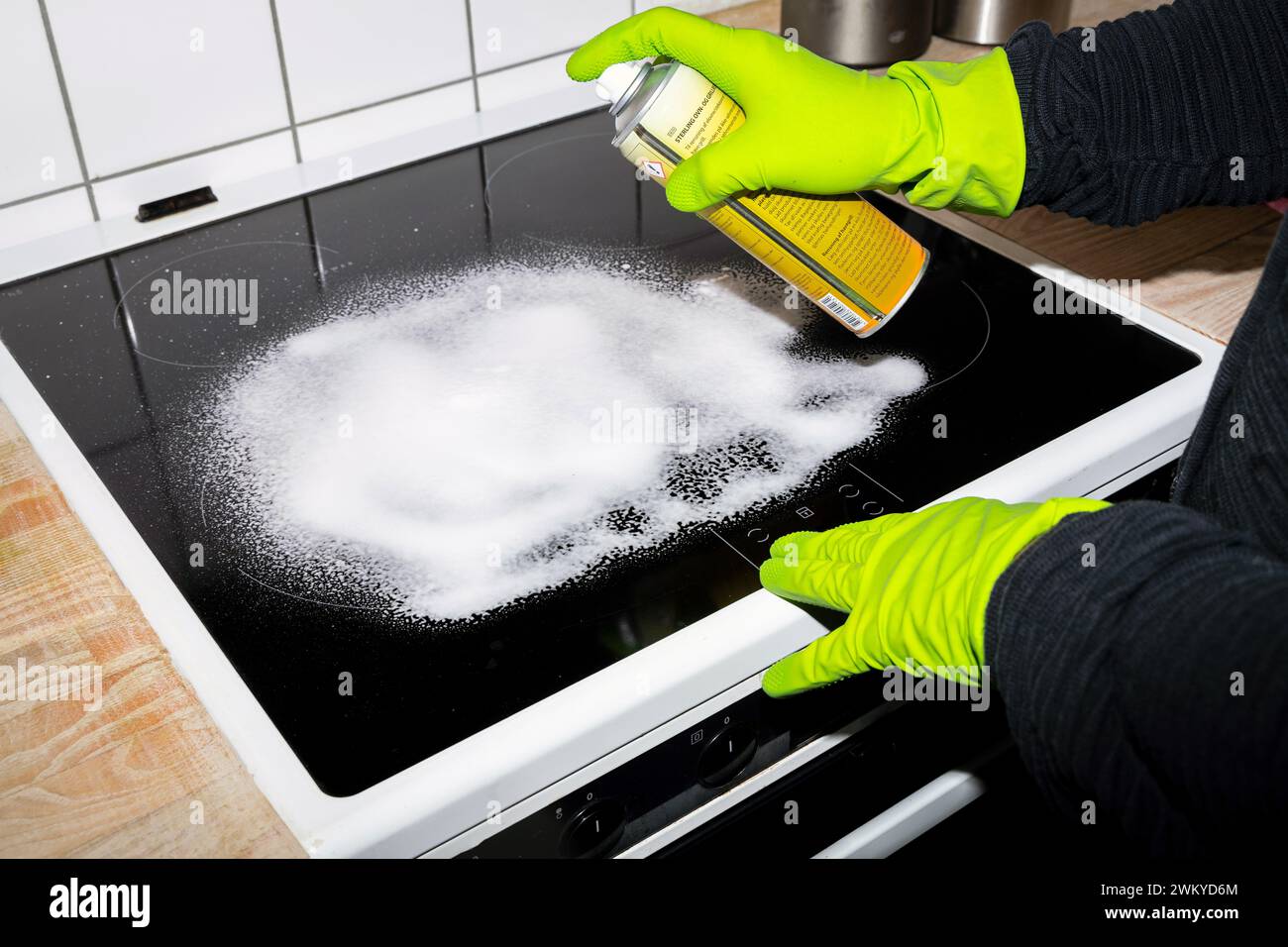 Eine Person in Gummihandschuhen, die das Induktionskochfeld reinigt und mit einem Tuch, einem Desinfektionsspray und einem Reinigungsmittel reinigt. Hausreinigung und Hygienekonzept. Stockfoto