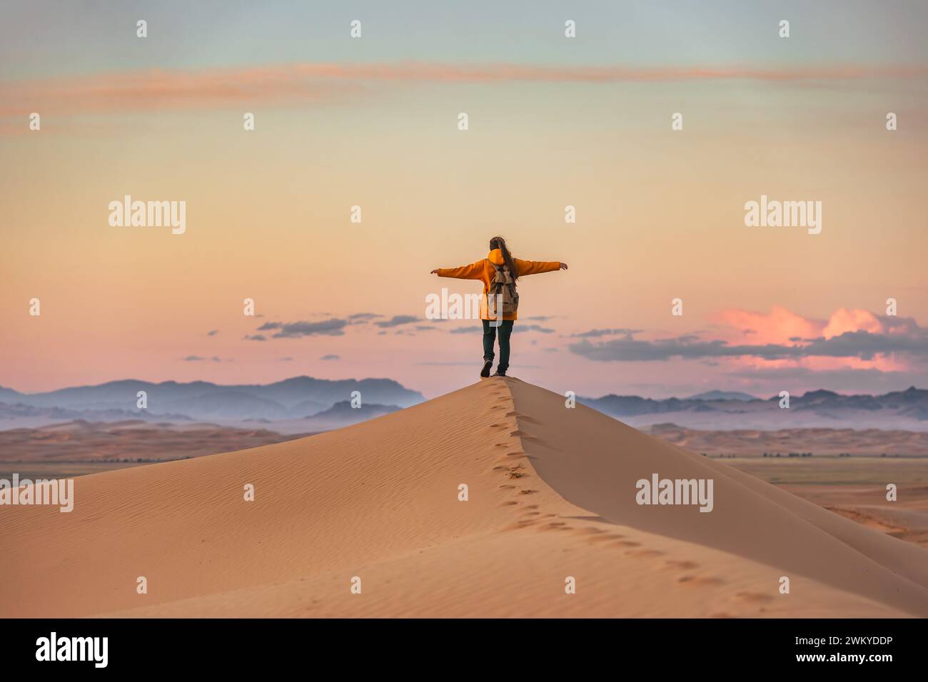 Glücklicher junger Wanderer steht mit offenen Armen an der Sanddüne und genießt den Sonnenuntergang Stockfoto