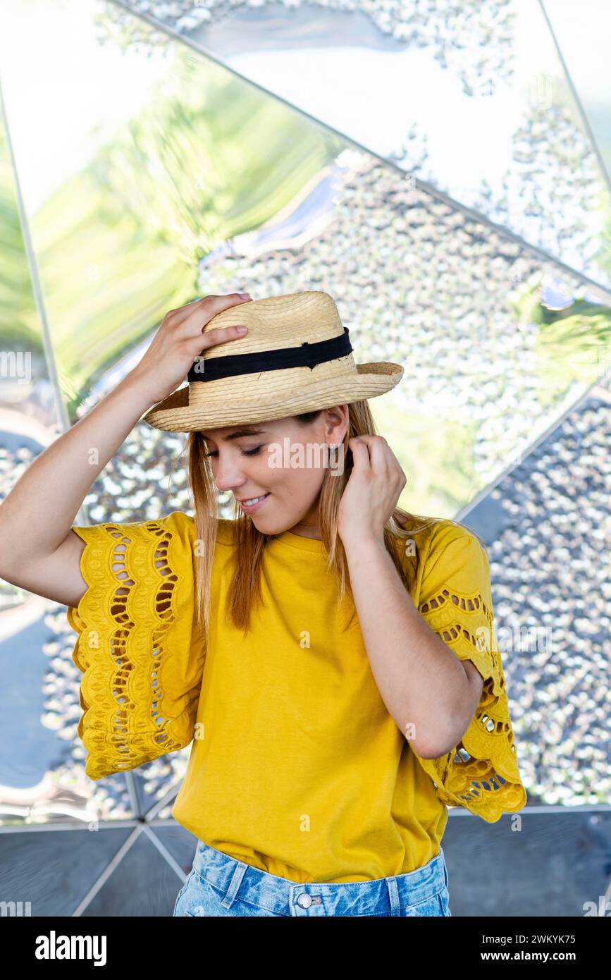 Auf diesem bezaubernden Foto passt eine junge Frau spielerisch einen Strohhut an und ergänzt ihre auffällige gelbe Bluse mit zarten Spitzendetails und Stockfoto