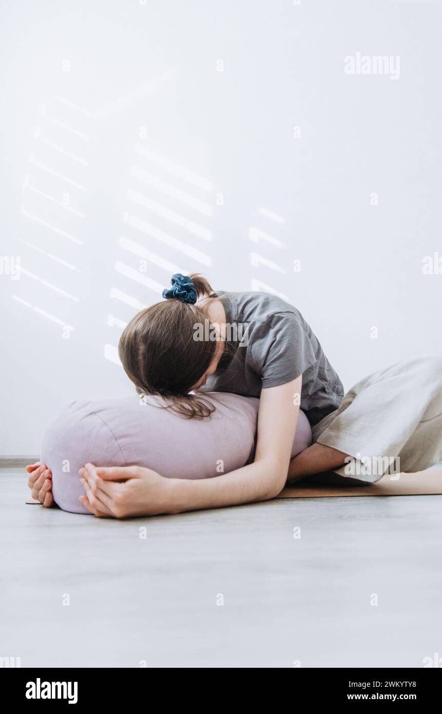 Frau in lässiger Kleidung übt Yin Yoga Schmetterling Pose mit Polster Stockfoto