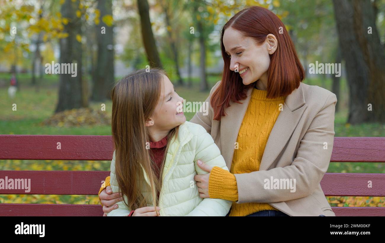 Glückliche Familie kaukasische Mutter mit kleiner Tochter umarmt lächelnd lachend auf der Parkbank Mama Babysitter Frau kuschelt umarmt sich mit dem liebenswerten Kind Stockfoto