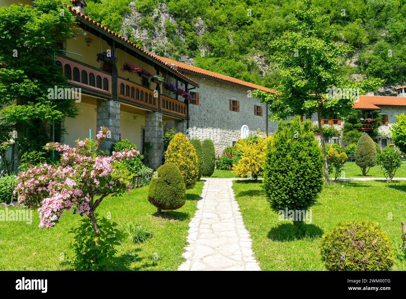 Malerischer Hof des Klosters von Moraca mit grünen Rasen, Blumen und Gebäuden mit roten Ziegeldächern vor blauem Himmel, Montenegro Stockfoto