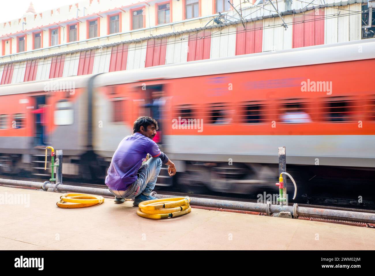 Ein Mitarbeiter der Indian Railways wartet auf einem Bahnsteig, als ein Zug vorbeifährt Stockfoto