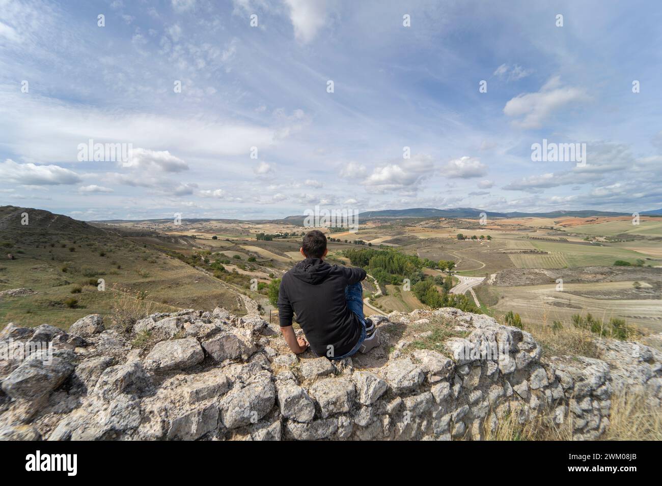 Aufmerksame Person in Sportbekleidung, die auf einem Felsen auf einem Aussichtspunkt sitzt und die weite Aussicht auf die Ebenen von castilla la mancha genießt. Stockfoto