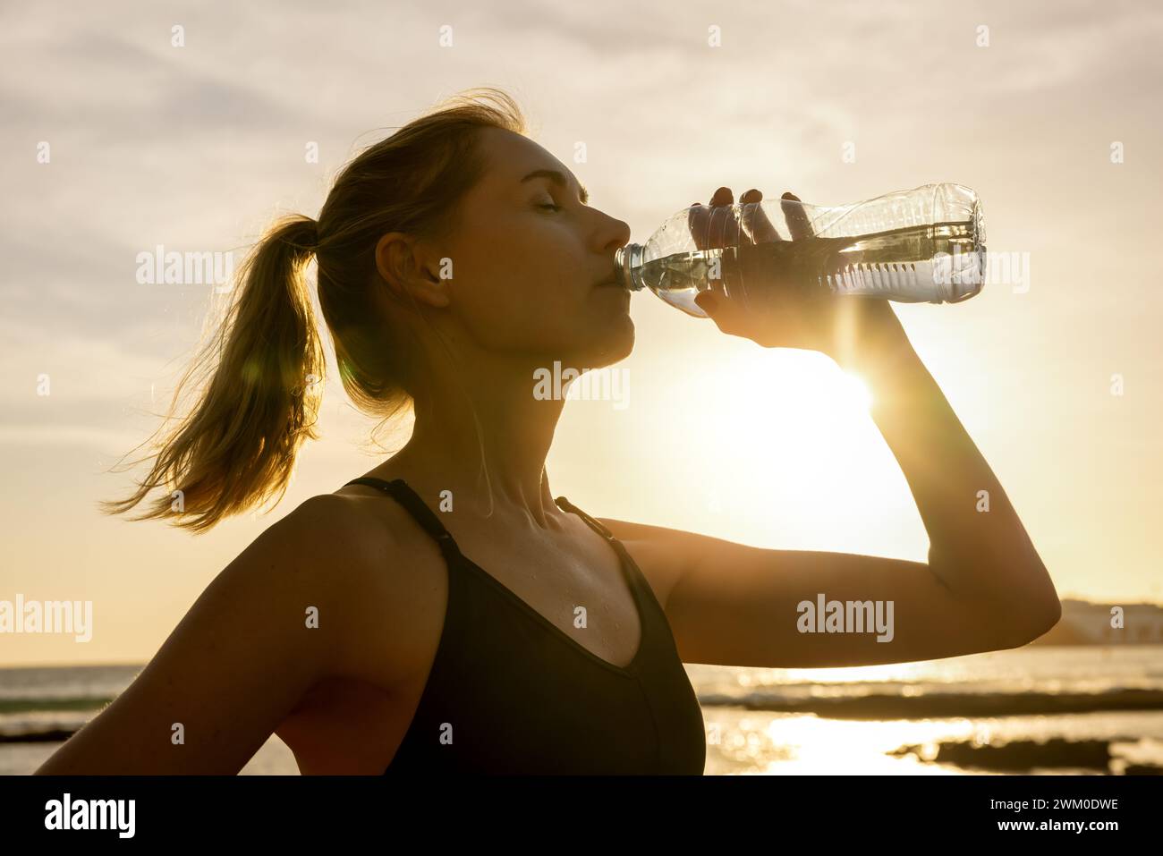 Sportliche Frau trinkt Wasser aus der Flasche nach dem Fitness-Workout im Freien bei Sonnenuntergang Stockfoto