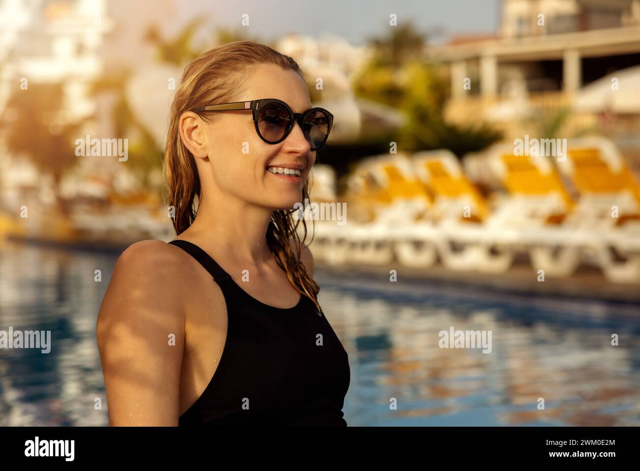 Frau, die bei Sonnenuntergang am Pool des Ferienortes sitzt und sich entspannt. Sommerurlaub Stockfoto