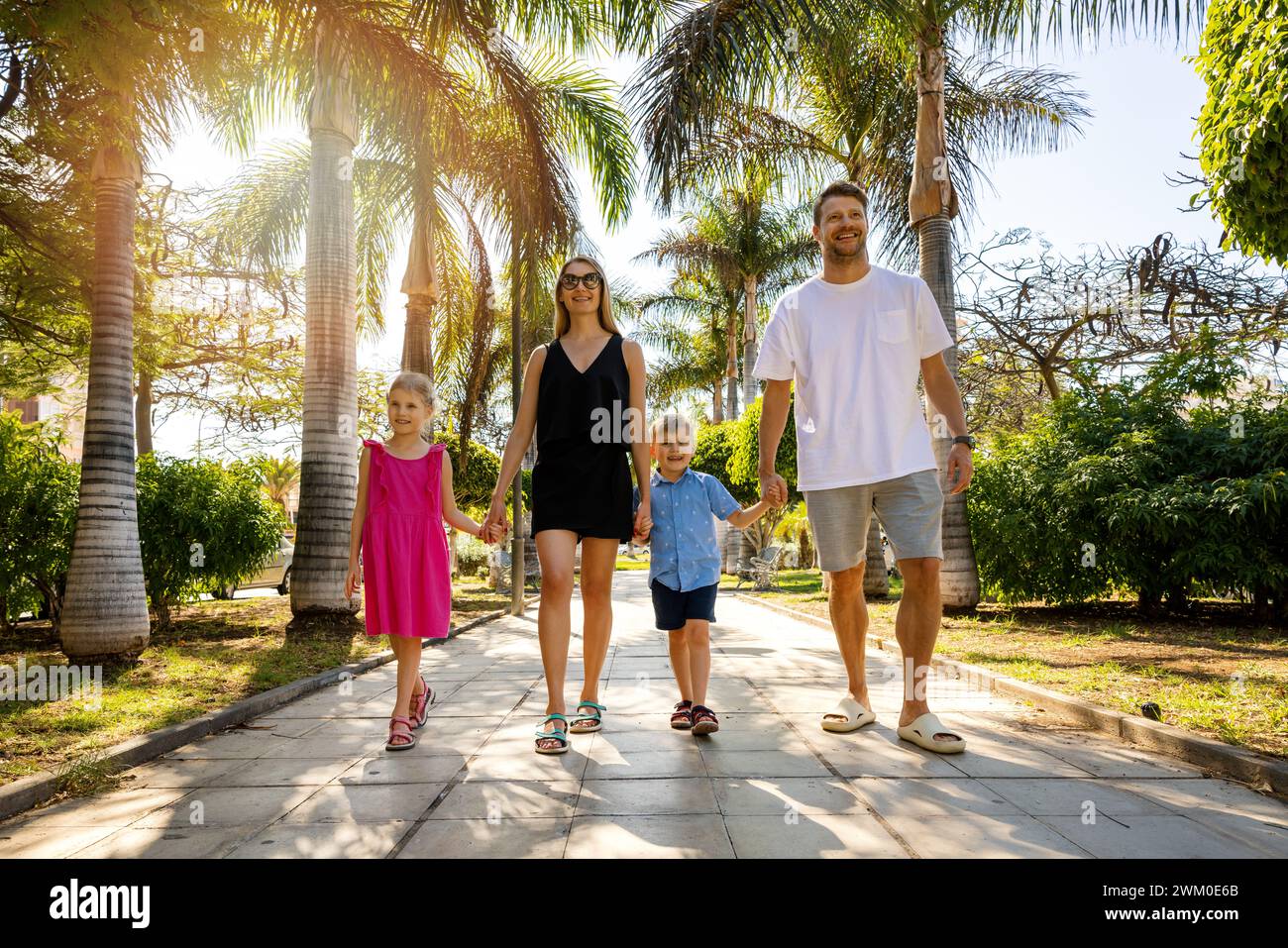 Glückliche Familie mit Kindern, die in einer Gasse in einem Palmenpark in Teneriffa, Spanien, spazieren gehen. Sommerurlaub Stockfoto