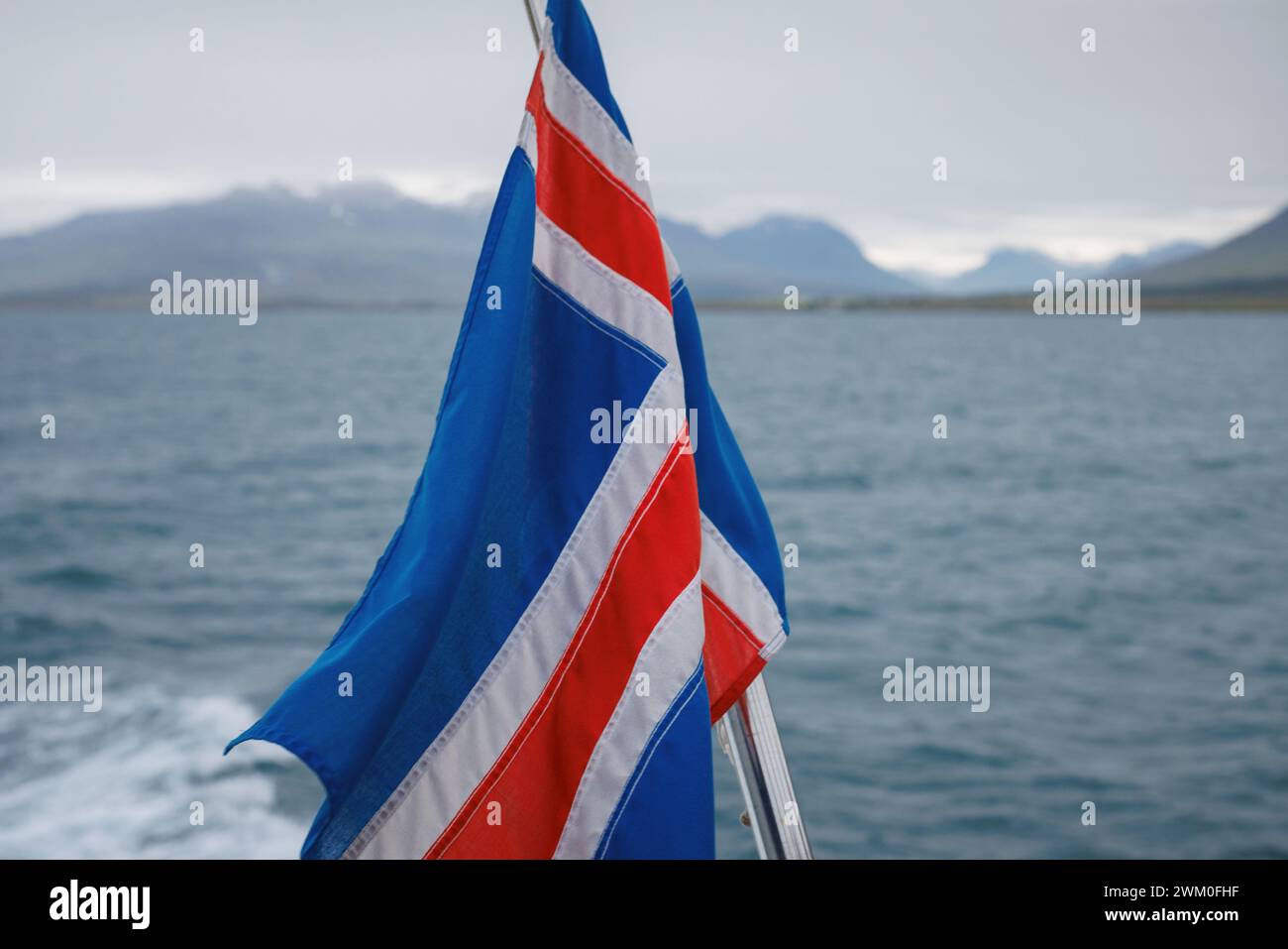Islandflagge auf dem fahrenden Boot im Meer mit einer wunderschönen Landschaft aus Bergen unter dem Schnee, dem Land des Feuers und des Eises. Reiseziel im Geheimen Stockfoto