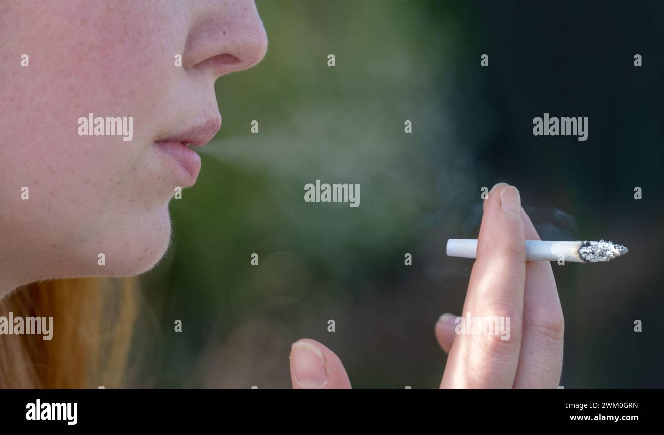 Porträt, Hand, Mund und Hand gezeichnete und handgerollte Zigarette einer jungen süchtigen Frau, die fröhlich den Rauch einer Zigarette raucht Stockfoto