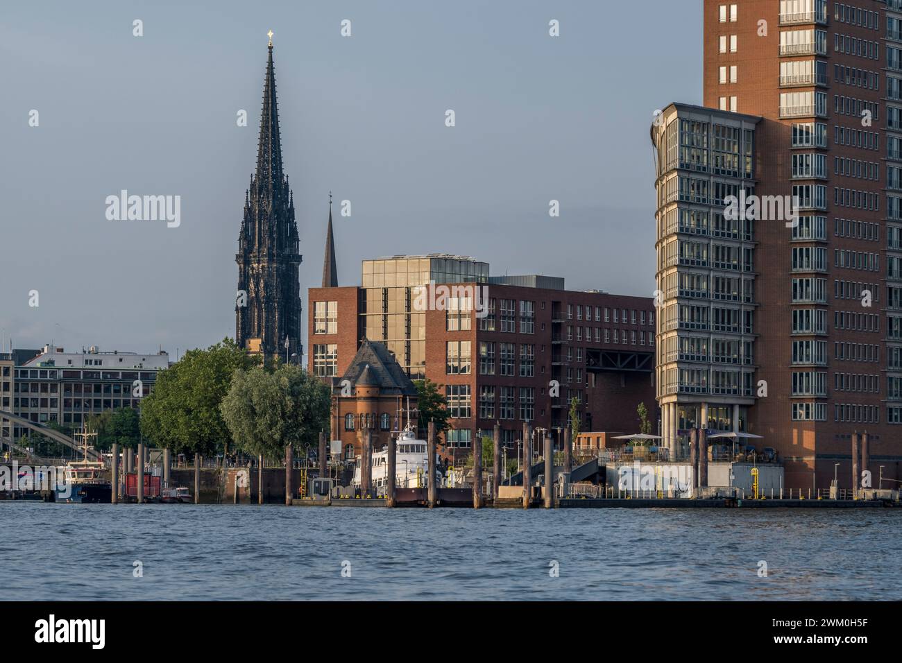 Deutschland, Hamburg, Gebäude am Flussufer mit Turm von St. Nikolaikirche im Hintergrund Stockfoto