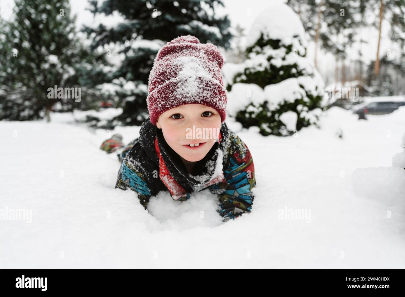 Verspielter Junge, der auf Schnee liegt Stockfoto