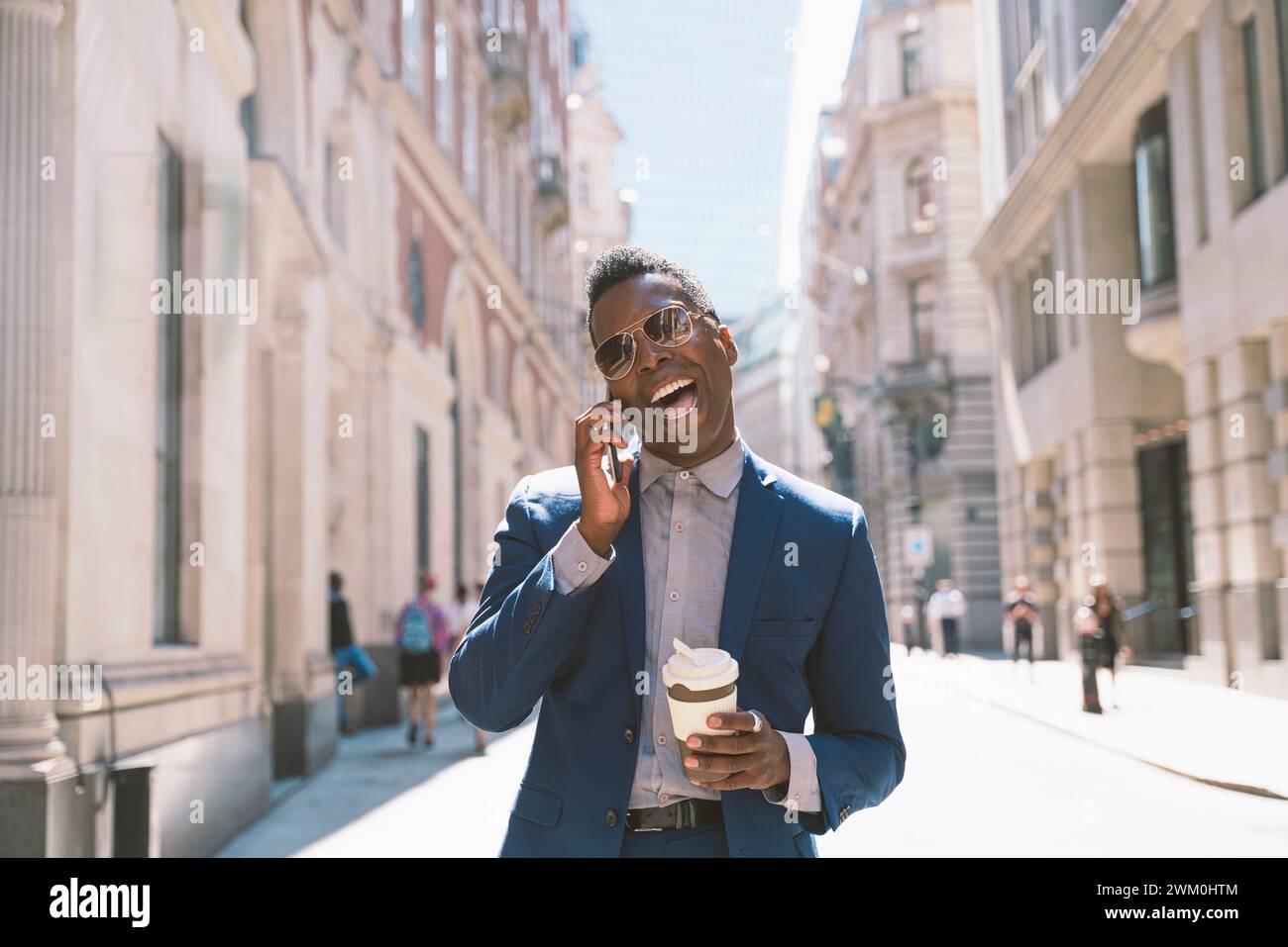 Fröhlicher Geschäftsmann, der eine Kaffeetasse hält und mit dem Smartphone spricht Stockfoto