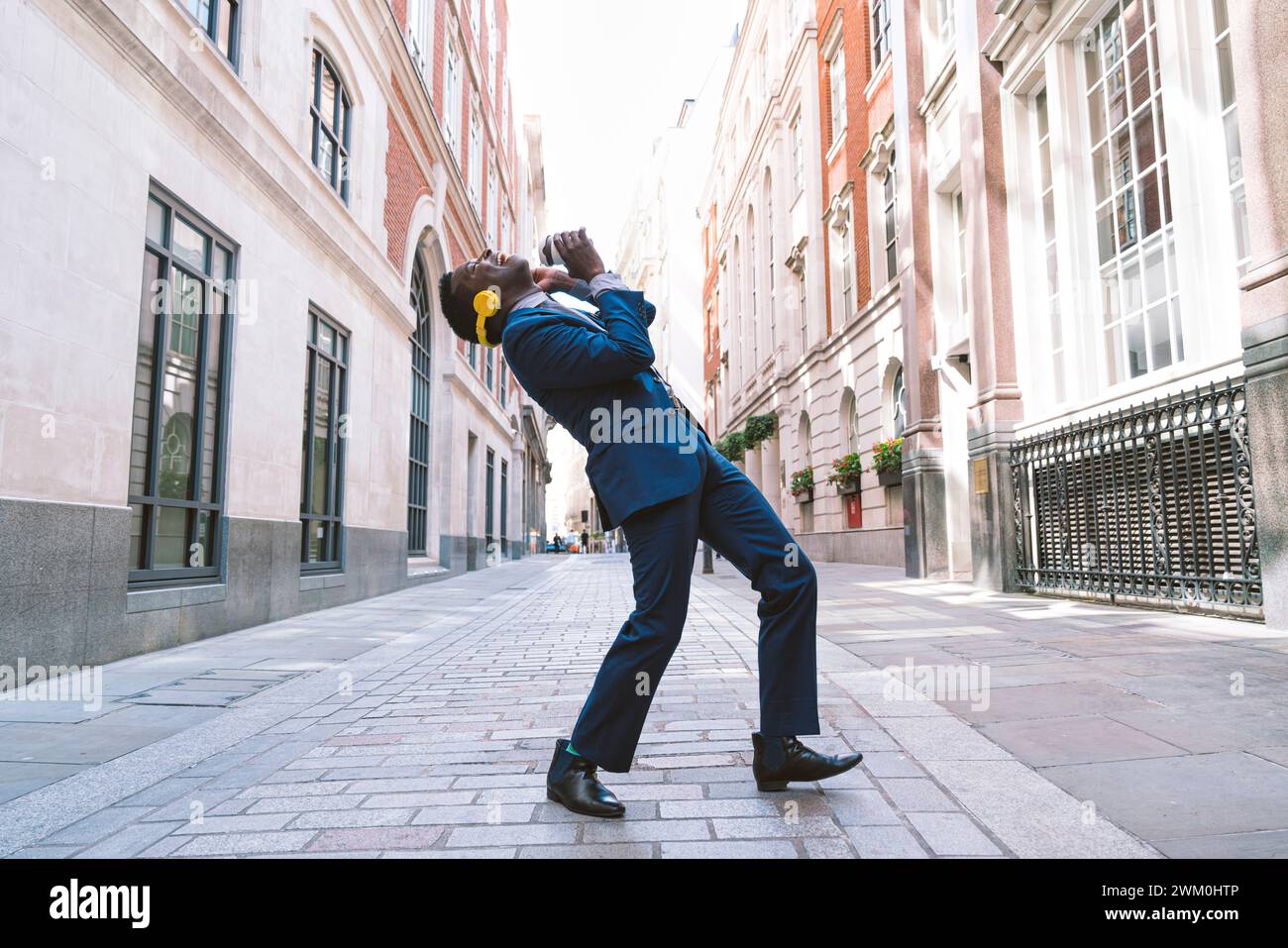 Fröhlicher Geschäftsmann, der kabellose Kopfhörer trägt und auf der Straße tanzt Stockfoto