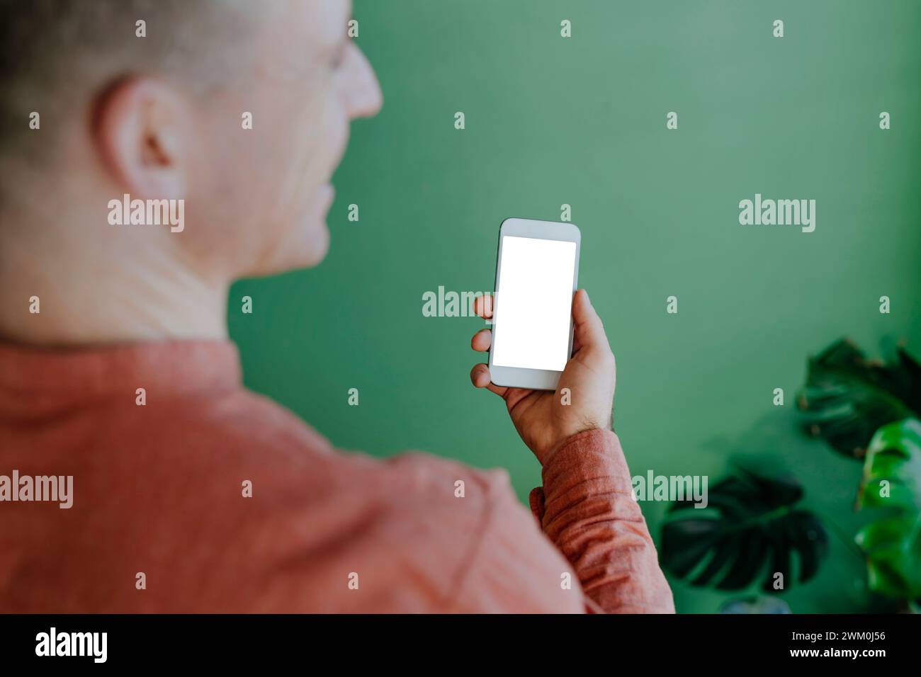 Mann, der ein Smartphone in der Nähe der grünen Wand hält Stockfoto