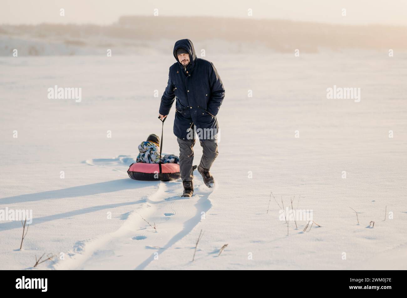 Mann zieht Jungen, der auf einem aufblasbaren Rohr im Schnee sitzt Stockfoto