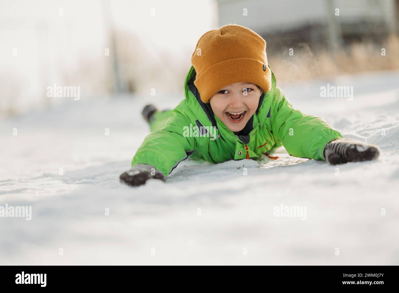 Fröhlicher Junge, der auf Schnee liegt Stockfoto