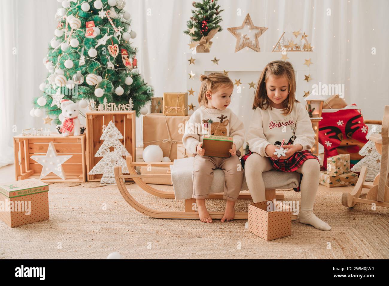 Glückliche Mädchen sitzen mit Geschenken in der Nähe der Weihnachtsdekoration zu Hause Stockfoto