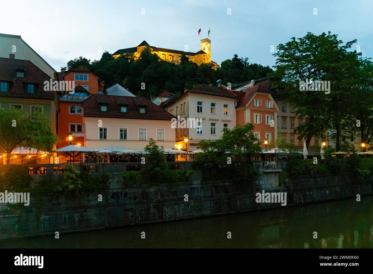 Slowenien, Ljubljana, Schloss Ljubljana mit Blick auf die Gebäude am Fluss in der Abenddämmerung Stockfoto