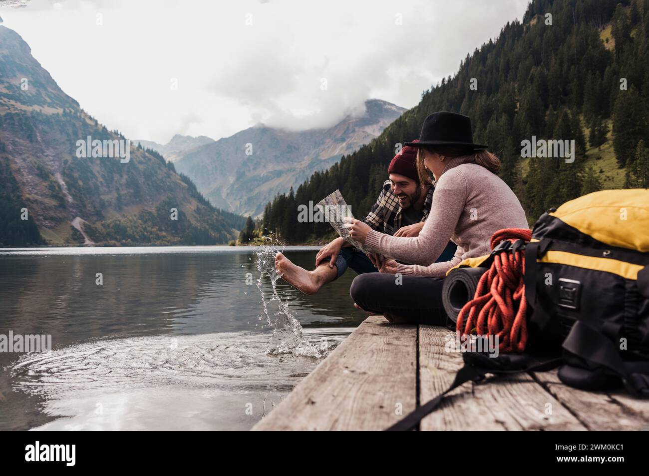 Glückliches Paar, das mit Karte auf dem Pier in der Nähe des Vilsalpsees und der Berge in Tirol, Österreich, sitzt Stockfoto