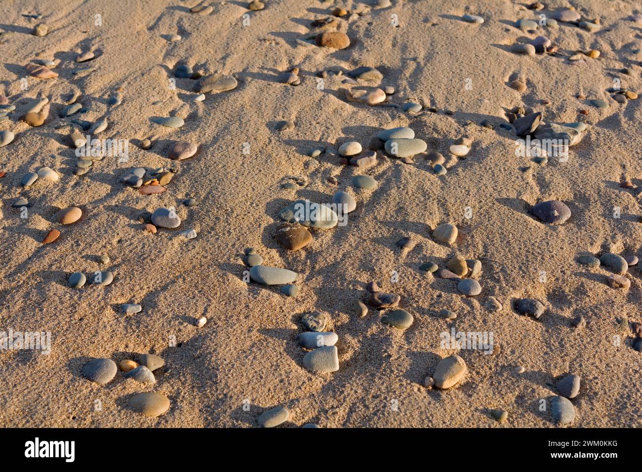 Kieselsteine am Sandstrand mit Schatten von niedriger Sonne Stockfoto