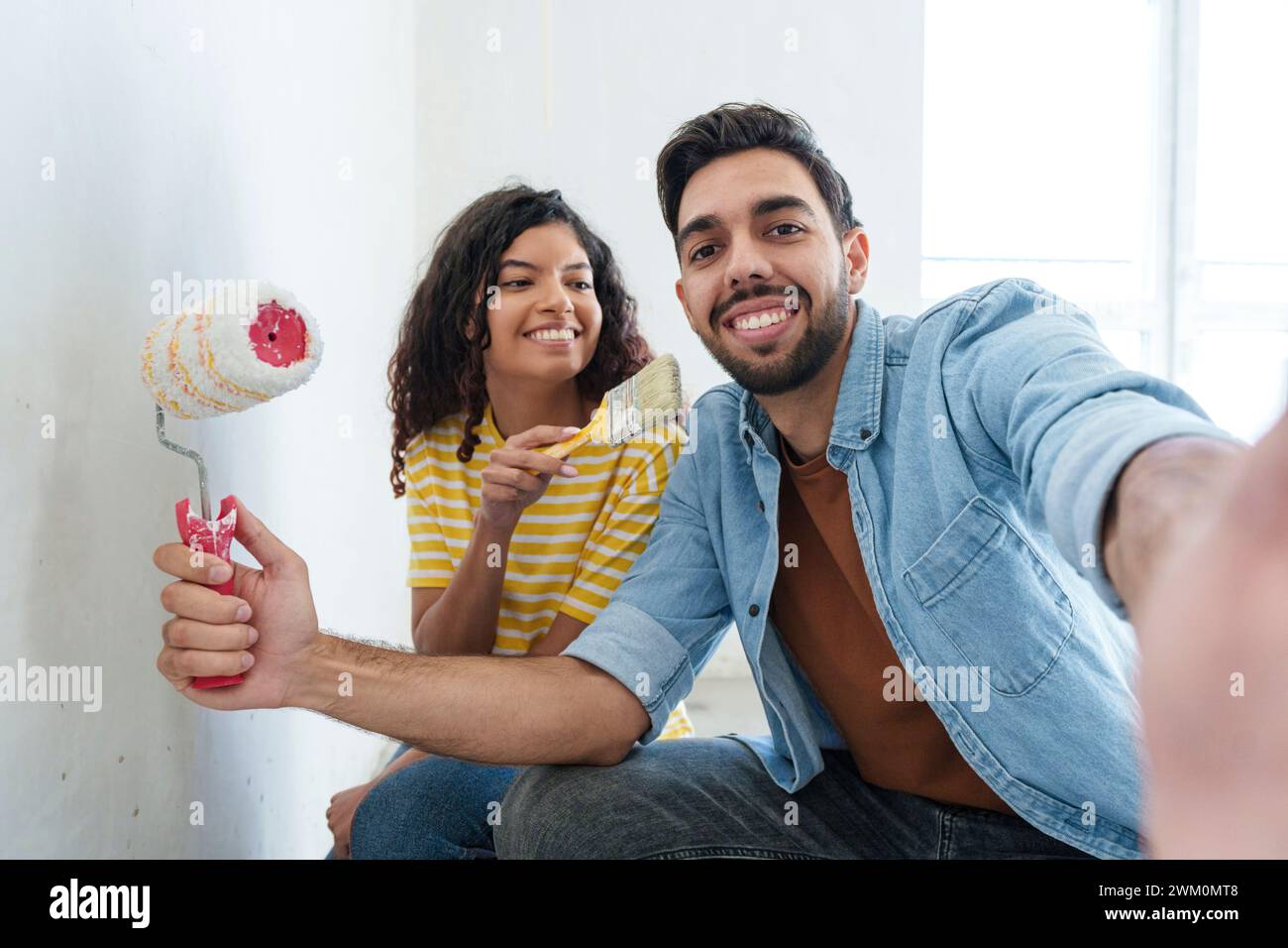Verspieltes Paar mit Malausrüstung, das Selfie in einem neuen Zuhause macht Stockfoto