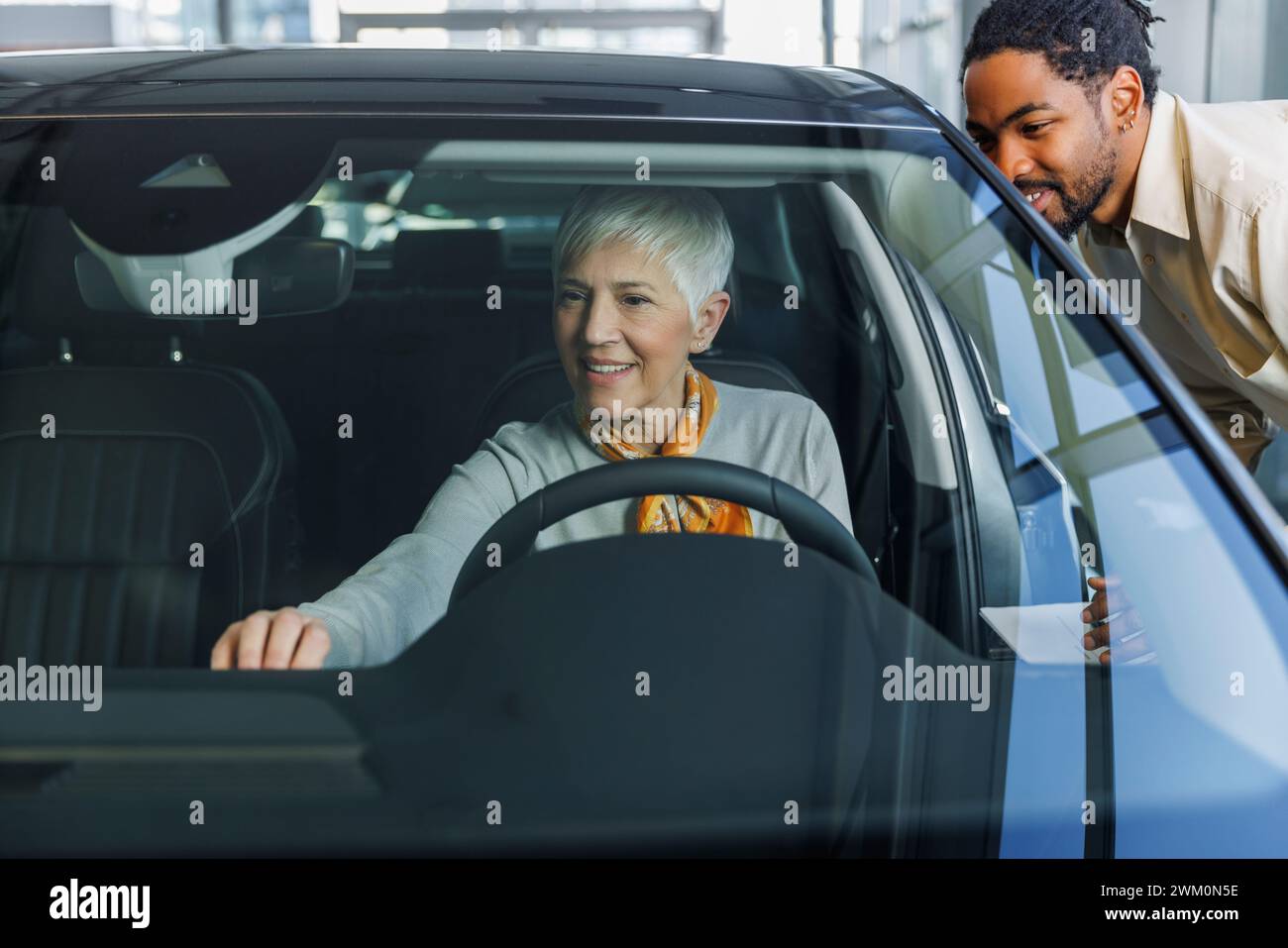 Lächelnder Verkäufer mit Frau, die das Auto im Ausstellungsraum untersucht Stockfoto
