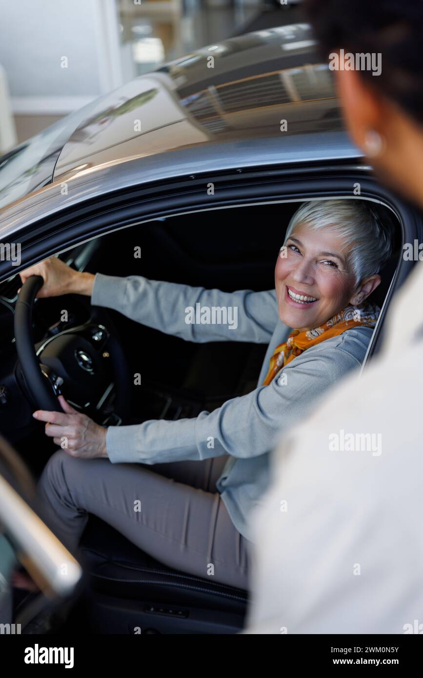 Glückliche Frau, die im Auto in der Nähe des Verkäufers im Ausstellungsraum sitzt Stockfoto