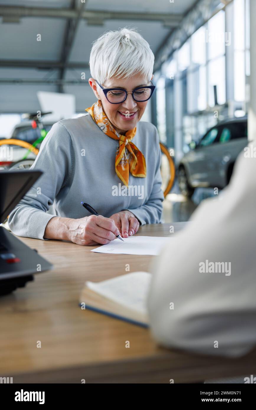 Lächelnder Kunde, der am Schreibtisch einen Kaufvertrag unterzeichnet Stockfoto